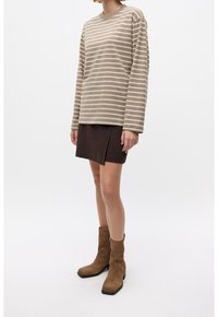 Top de manga larga a rayas beige y crema combinado con una falda marrón oscuro. La modelo lleva botas de ante marrón hasta el tobillo con tacón ancho.