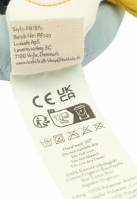 Etichetta per un peluche: tessuto crema con accenti gialli e blu, istruzioni per la cura e dettagli sui materiali che includono cotone biologico e poliestere.