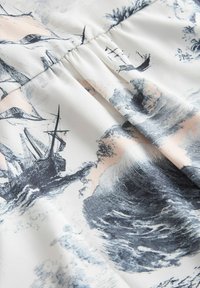 Witte stof met een nautische print in blauw en roze, met zeilschepen, oceaangolven en meeuwen in een schetsachtige stijl.