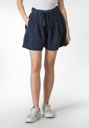 Pantaloni di lino blu navy con vita elasticizzata, dettaglio con fiocco, pieghe sul davanti e tasche laterali, abbinati a sneakers chiare.