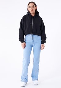 Black cropped hoodie with a zipper and drawstrings, paired with light blue jeans. White sneakers complete the casual outfit.