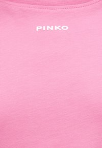 Ροζ ύφασμα με ραμμένη γραμμή λαιμού και λευκά κεφαλαία γράμματα "PINKO" κεντραρισμένα κοντά στον γιακά.