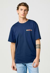 Mörkblå bomulls-t-shirt med korta ärmar och rund halsringning, med en färgglad "WRANGLER"-logotyp på vänster bröst.