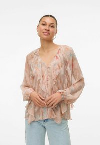 Blusa trasparente color pesco con fronte e maniche arricciate, dotata di scollatura a V e chiusura con bottoni. Leggeri motivi floreali in tonalità di rosa e blu.