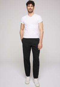 T-shirt bianca a collo a V, pantaloni neri aderenti e sneakers bianche. Tessuto morbido, design aderente, con tasche frontali e un look minimalista.