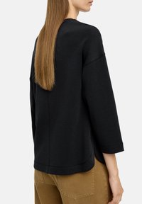 Czarny sweatshirt o luźnym kroju, z rękawami 3/4 i zaokrąglonym dołem. Wykonany z miękkiego, teksturowanego materiału. Prosty design, bez widocznych wzorów.