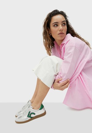 Zapatillas plateadas metálicas con acentos de purpurina verde, que presentan una suela texturizada y un diseño clásico con cordones, combinadas con una camisa oversized rosa.