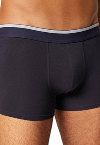 Boxer in cotone nero con elastico blu scuro con una striscia grigia chiara. Il tessuto appare liscio e aderente alla pelle.