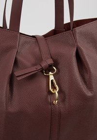 Sac à main en cuir texturé marron foncé avec deux anses et une boucle métallique dorée fixée à une boucle en cuir à l'avant.