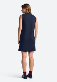 Námornícka tmavomodrá šaty bez rukávov s priamym strihom, okrúhlym výstrihom a hladkou textúrou. Nosené s bordovými ponožkami a čiernymi topánkami.