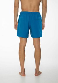 Blå badshorts tillverkade av lättviktigt tyg, med resårmidja och en bakficka med en liten logotagg.