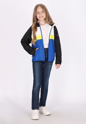 Giacca con zip blu e nera con una striscia gialla, abbinata a jeans in denim e sneakers bianche. La giacca è dotata di cappuccio e tasche.