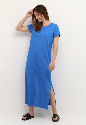 Robe maxi bleue à manches courtes, fabriquée en tissu lisse. Présente des fentes latérales et un col rond. Portée avec des sandales noires.