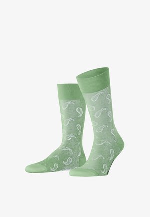 Een paar lichtgroene, semi-transparante sokken met witte paisley-patronen en effen boorden, hielen en tenen, naast elkaar gelegd.