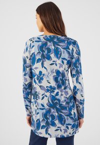 Maglia a maniche lunghe in tessuto grigio chiaro con un motivo floreale blu. Il design include grandi fiori e foglie in diverse sfumature di blu.