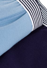 Due sezioni di tessuto: una di un blu chiaro e l'altra di un blu navy scuro. La sezione blu presenta una texture liscia, mentre quella navy è leggermente pelosa. Inclusa una fascia elastica a righe.