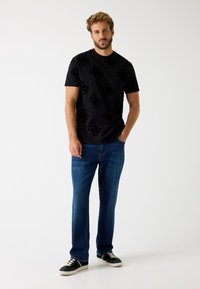 Sort kortærmet t-shirt med et diskret præg mønster, parret med blå denim jeans og sorte sneakers med en hvid sål.