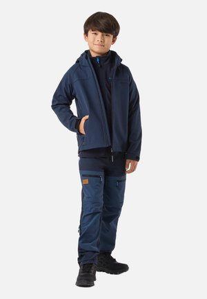 Boy standing in navy outdoor jacket, matching cargo pants with multiple zippered pockets, and black hiking boots on white background.