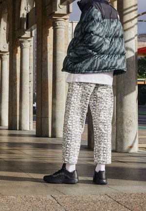 Puffer jacket in dark teal with a textured pattern, paired with white pants featuring a black graphic print and black sneakers.