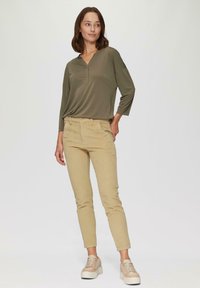 Olivenfarbener langärmeliger Oberteil mit V-Ausschnitt, kombiniert mit beigen Slim-Fit-Hosen und hellen Sneakers. Glatte Textur und lässiges Design.