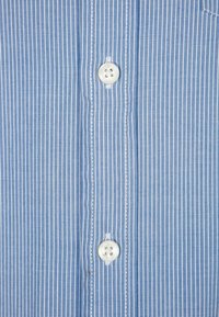 Vaaleansininen raidallinen paita, jossa pystysuorat viivat, valkoiset napit ja sileä kangaspinta sekä tavallinen kaulustyyli.