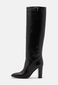 Botte en cuir noir, montante jusqu'au genou, avec un bout pointu et un talon bloc. Présente un accent doré en forme de 'T' en haut, texture lisse tout au long.