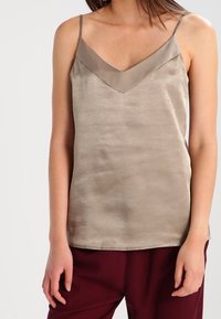 Béžový saténový top s véčkovým výstřihem, nastavitelnými špagetovými ramínky a hladkou texturou, doplněný tmavě vínovými kalhotami.