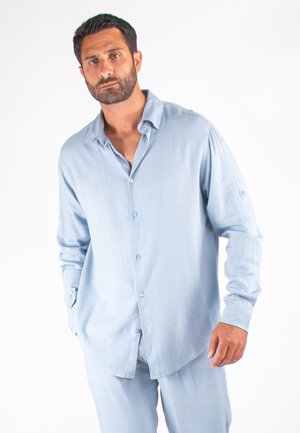 Chemise à manches longues bleu clair en tissu doux, dotée d'un devant à boutons, d'un col pointu et d'une coupe décontractée avec des manches retroussées.