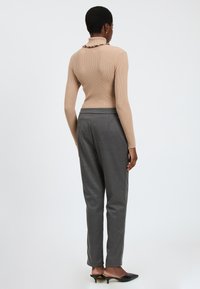 Beige geribbelde coltrui met ruches bij de kraag, gecombineerd met grijze op maat gemaakte broeken en zwarte hakschoenen, gezien vanuit de rug.