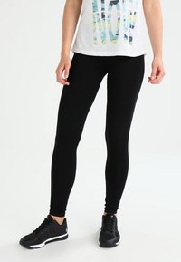 Leggings noirs en tissu extensible, design ajusté, longueur cheville. Associés à un haut blanc ample avec un texte coloré et des baskets noires.