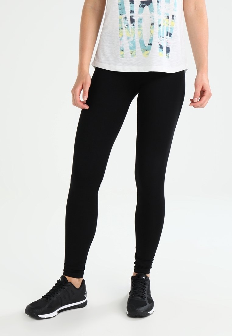 Leggings noirs en tissu extensible, design ajusté, longueur cheville. Associés à un haut blanc ample avec un texte coloré et des baskets noires.