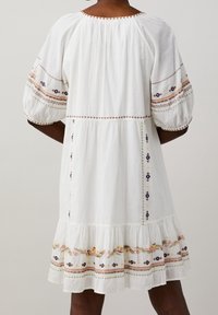 Vit bomullsklänning med puffärmar, blommig broderi i rosa, gult och blått, flerlagrad volangkant och en avslappnad passform.