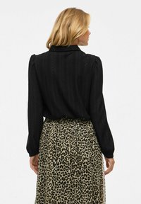 must värvi tekstuuriga pluus, millel on pufed varrukad ja kraega kaelus, kombineeritud voolava leopardimustriga seelikuga, millel on elastne vöökoht.