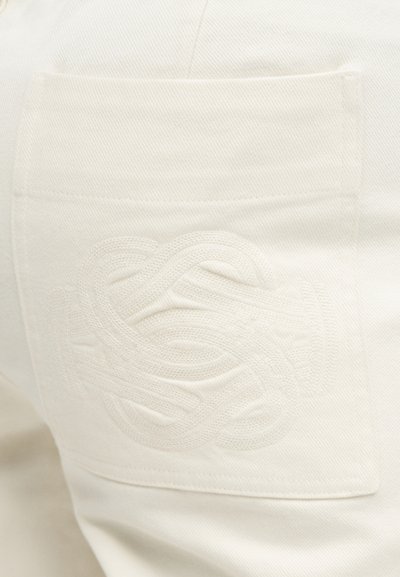 Κοντινό πλάνο σε λευκό ύφασμα τζιν με πίσω τσέπη που έχει ανάγλυφο, περίπλοκο λευκό κεντητό σχέδιο κόμπου.
