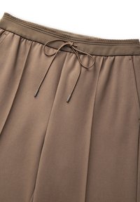 Brązowe dresy z elastycznym pasem na sznurek, plisowanym wzorem i gładką strukturą. Materiał jest miękki i lekki.