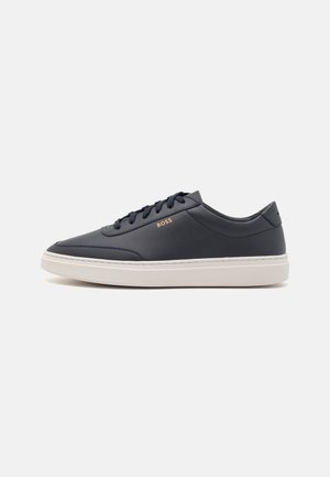 Baskets basses en cuir noir avec semelle blanche et lacets noirs, avec le logo doré "BOSS" sur le côté.