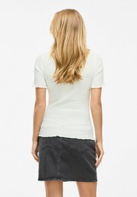 Vit strukturerad kortärmad topp i kombination med en svart denimkjol, som har en vågig nederkant och två bakfickor.