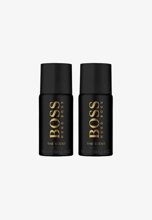 Sorte cylindriske beholdere af deodorant med guldtekst, der læser "BOSS HUGO BOSS THE SCENT." Hver flaske rummer 150 ml.