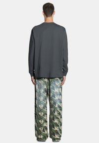 Szara, długorękawowa koszula zestawiona z zielonymi spodniami w stylu kamuflażu o szerokich nogawkach, prezentująca swobodny fason z miękkiego materiału i widocznymi detalami tekstury.