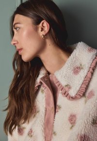 Fleecejakke med hvid bundfarve, pink blomstermønster og en rynket pink krave. Tekstureret stof med kordfløjl knaplukning.