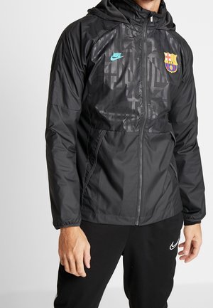 Mand iført sort Nike FC Barcelona hættetrøje og sorte Nike bukser, stående med hænderne afslappet ned langs siden.