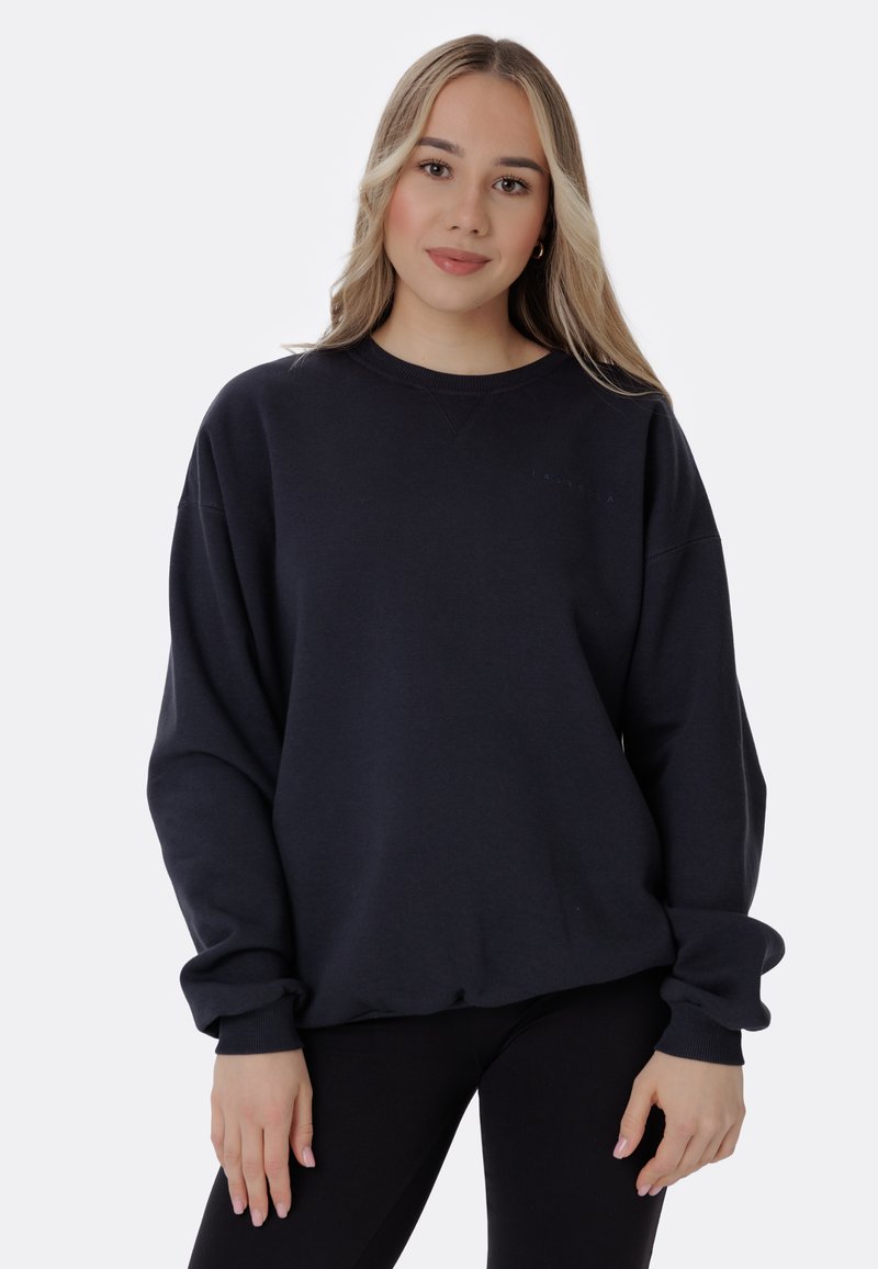 Felpa nera oversize con maniche lunghe e polsini a costine. Presenta un colletto rotondo e un piccolo logo discreto sul petto.