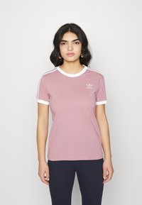 Šviesiai rožinė medvilninė marškinėliai su balta apykakle ir rankovių akcentais. Pasižymi Adidas logotipu kairėje krūtinės pusėje ir trimis baltomis juostelėmis ant pečių.