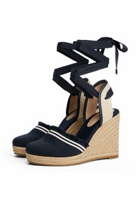 Navy canvas wedge sandals with a braided jute heel, elastic straps, frayed edges, and contrasting white stripes. Textured side panels.