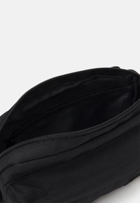 Czarna torba materiałowa o gładkiej teksturze, z zamknięciem na zamek i wewnętrzną przegrodą z dodatkową kieszenią na zamek dla lepszej organizacji.