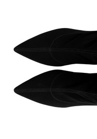Czarne szpiczaste buty wykonane z miękkiego materiału, z widocznym przeszyciem wzdłuż szwów oraz eleganckim, zwężonym designem.