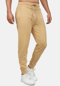 Beige joggers met een elastische tailleband, striksluiting, zijzakken en geribd manchetten, gecombineerd met witte sportschoenen.