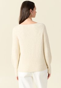Maglione a coste di colore crema, con scollatura ampia, maniche lunghe e vestibilità rilassata. Texture morbida con una leggera lucentezza.