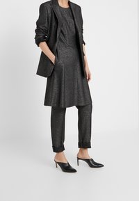 Czarny, metaliczny materiał w zestawie składającym się z sukienki do kolan z dopasowanym gorsetem i luźną spódnicą, w połączeniu z tapered, podwiniętymi spodniami oraz butami na obcasie.