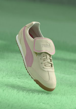 Beige mokkasneaker med rosa detaljer, rund tå, snøringssystem og en borrelåsrem, med en logo på tungen og en teksturert såle.